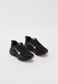 Black athletic shoes with a breathable mesh upper, white Nike swoosh, textured sole, and contrasting brown accents. Includes reinforced heel.