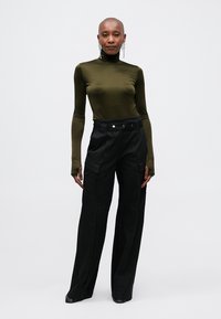 Olive green long-sleeve top paired with high-waisted black wide-leg pants featuring front pockets and button details. Smooth fabric texture.