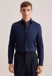 Camicia a maniche lunghe blu navy con colletto a punta, chiusura con bottoni e texture liscia; abbinata a pantaloni scuri, design semplice, senza motivi.