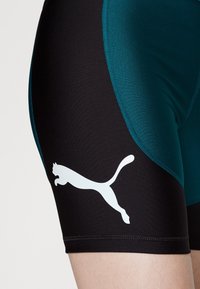 Bañadores deportivos de Puma, con una base negra y paneles en color teal, hechos de material elástico; incluyen un logo blanco de Puma en el muslo.