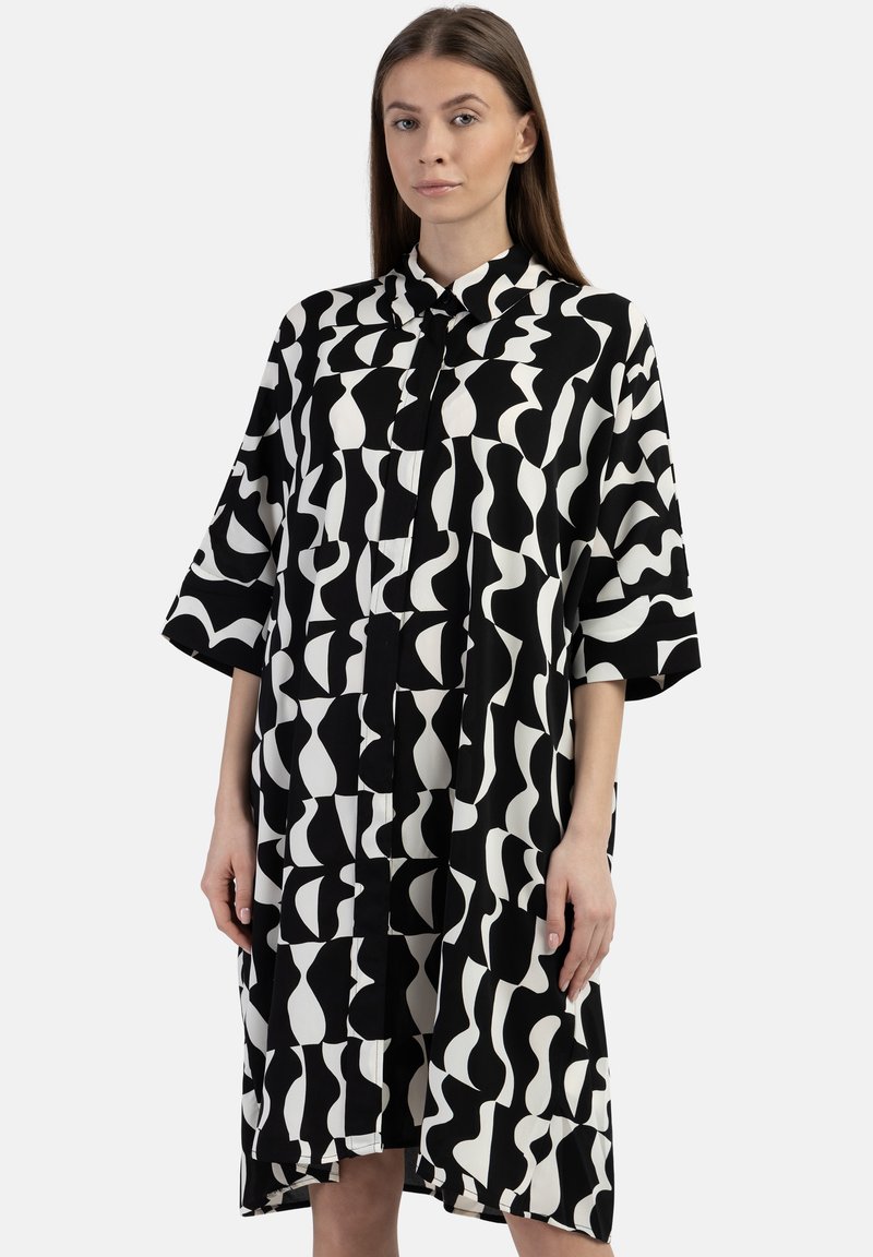 Schwarz-weißes Kleid mit einem auffälligen abstrakten Muster, kurzen Ärmeln, einem Kragen und einem geraden Schnitt mit seitlichen Schlitzen. Glatte Stofftextur.