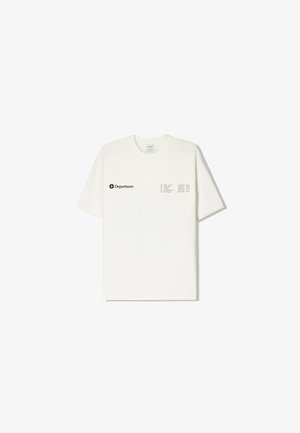 Tricou din bumbac crem cu mâneci scurte, cu text negru și un design în grilă pe partea stângă, guler rotund și o croială lejeră.