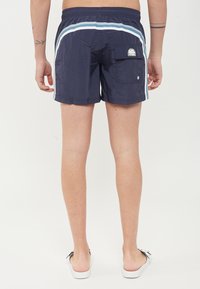 Pantaloni da nuoto navy con cintura elastica, strisce azzurro chiaro a contrasto e tasca posteriore con patch logo. Tessuto leggero.