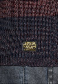 Maglione lavorato a maglia con strisce di un blu navy scuro e bordeaux, caratterizzato da un motivo testurizzato. Include un'etichetta rettangolare con i dettagli del marchio e lo slogan.