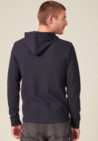 Felpa con cappuccio blu navy e maniche lunghe, realizzata in tessuto testurizzato. Caratterizzata da una tasca a canguro e polsini a coste sulle maniche.