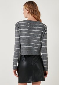 Szürke csíkos pulóver, amely cropped fazonú és puha textúrájú, egy fekete bőr szoknyával párosítva, kortárs stílusért.