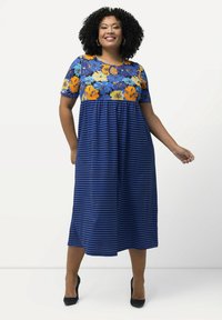 Vestido maxi con un top de estampado floral en azul y naranja, mangas cortas y una falda a rayas en color marino. Detalle en forma de ojal en el escote.