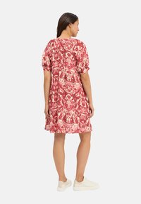 Red and cream patterned dress with puffed sleeves, relaxed fit, and a gathered back detail; paired with light-colored sneakers.