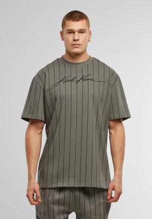 Short-sleeve, olive green T-shirt with black vertical stripes and a signature graphic on the front. Made of soft fabric, relaxed fit.