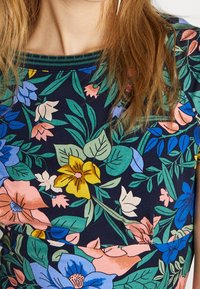 Bloemenbedrukte top met een marineblauwe achtergrond, multikleurige bloemen en groene bladeren. Ribbelhals, korte mouwen, katoenen stof.