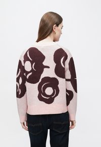 Pleteni pulover v mehki roza barvi z velikimi temno bordo cvetličnimi vzorci. Ima rebraste manšete in pas, ki nudijo sproščen oprijem.