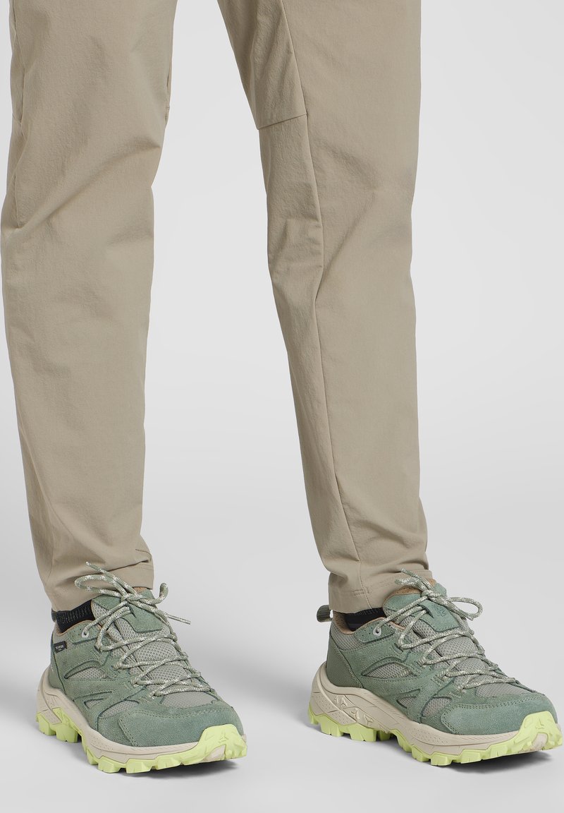 Groene wandelschoenen met grijze accenten, textuur oppervlaktes en een dikke, tractiongerichte zool in lichtgeel, gecombineerd met beige broek.