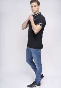 Camisa polo negra con cuello a rayas blancas y grises, combinada con jeans de mezclilla azules y zapatillas negras con acentos blancos.