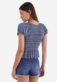 Blue, smocked blouse with short puff sleeves, peplum hem, and patterned texture, paired with denim shorts.