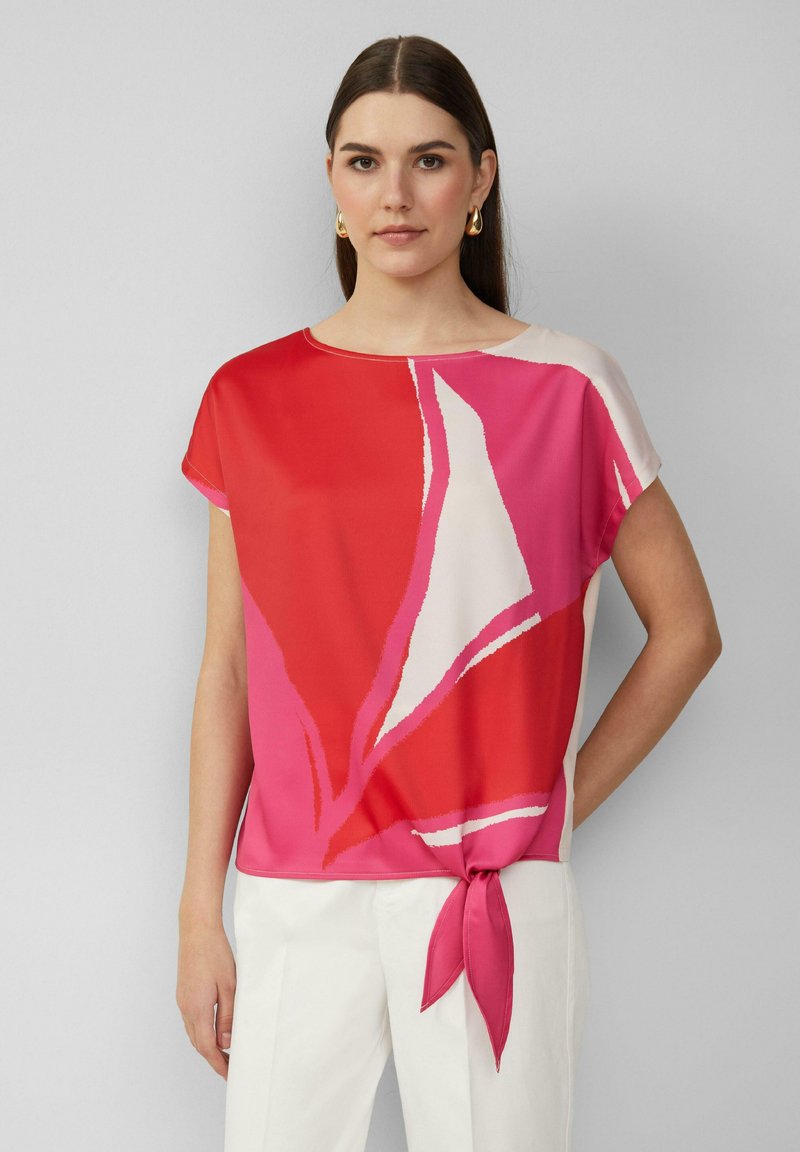 Rode en roze gebloemde blouse met korte mouwen, een ronde halslijn en een strikaccent ter hoogte van de taille, gemaakt van een gladde, lichte stof.