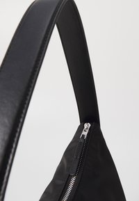Black synthetic handbag with a smooth texture, angular shape, and a wide strap. Features a silver zipper with a leather pull accent.