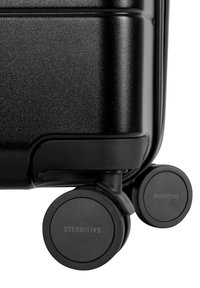 Schwarzer Hartschalenkoffer mit strukturierten Oberflächen, ausgestattet mit vier robusten schwarzen Rollen und mit "ETERNITIV3" in die Radnaben eingraviert.