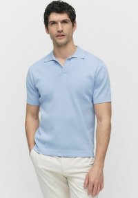 Ljusblå kortärmad polo med en mjuk textur, som har en klassisk krage och en rak fåll, bärs med ljusa byxor.