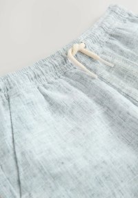 Shorts en lin bleu clair avec une taille élastique et un cordon de serrage beige. Présente une surface texturée et des plis avant pour le détail du design.