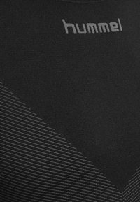 Musta urheilupaita, joka on valmistettu joustavasta kankaasta. Paidassa on harmaa "hummel"-logo ja kevyempiä vinoraitakuviota.