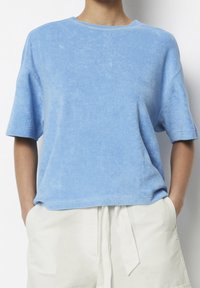 Blå bomullst-shirt med korta ärmar, rund halsringning och mjuk textur. Har en avslappnad passform och ett subtilt blekt mönster.