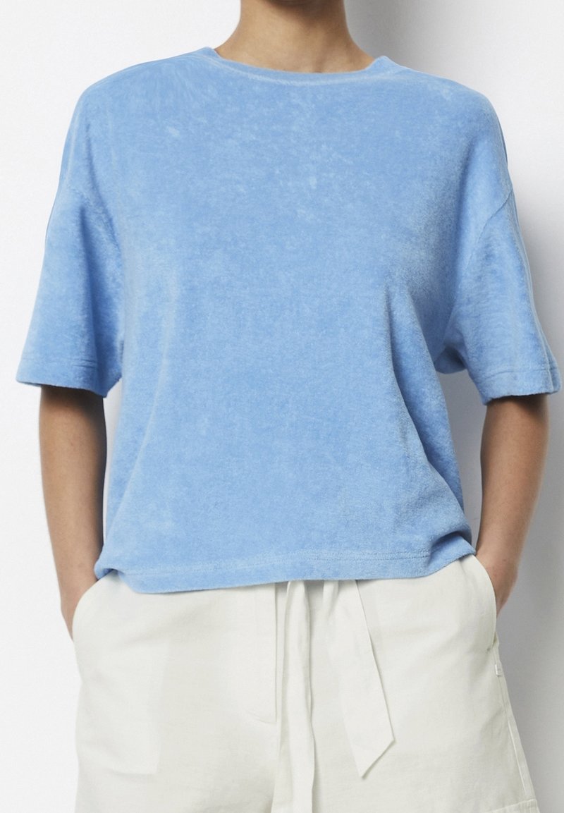 Blå bomullst-shirt med korta ärmar, rund halsringning och mjuk textur. Har en avslappnad passform och ett subtilt blekt mönster.