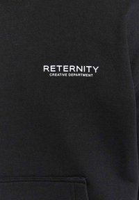 Tessuto nero con testo bianco che recita "DEPARTAMENTO CREATIVO RETERNITY" sopra una cucitura orizzontale o il bordo di una tasca.