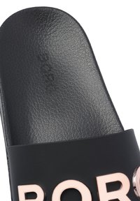 Gros plan d'une sandale noire à enfiler avec une semelle intérieure texturée et de grandes lettres en relief rose pâle sur la bride.