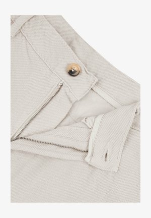 Pantaloni beige in cotone con zip e chiusura a bottone. Tessuto testurizzato con dettagli a righe diagonali.