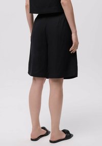 Zwarte shorts met een losse fit, knielange zoom en zijzakken. Draag ze met zwarte instapsandalen die een eenvoudig ontwerp hebben.