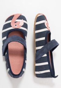 Kankaat kengät tummansinisillä ja valkoisilla raidoilla, vaaleanpunainen flamingosovellus varpaassa ja tarranauha turvalliseen kiinnitykseen.