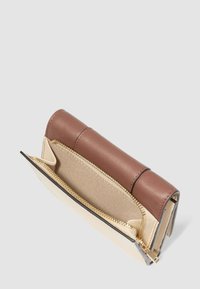 Portafoglio in pelle marrone e beige aperto per mostrare il compartimento interno con zip dorata, su uno sfondo chiaro e semplice.