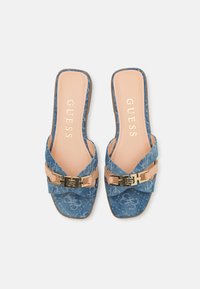 Denim open-toe sandals with a light blue fabric upper, featuring a crisscross design and gold-tone hardware detailing. Flat sole, brand logo visible.