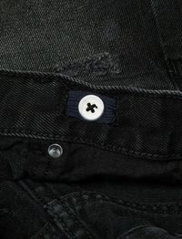 Tissu en denim noir avec des coutures visibles. Comprend un bouton blanc avec un onglet en tissu marine. Comprend un bouton-pression argenté et des détails usés.