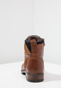 Botte chelsea en cuir marron avec un panneau en daim, un col en tissu marine et une doublure à carreaux. Comprend une fermeture éclair à l'arrière et une semelle en caoutchouc texturée.