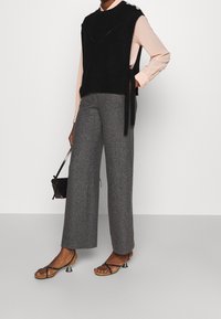 Un pull sans manches en tricot noir porté sur une chemise rose pâle, associé à un pantalon large à carreaux vichys gris et des sandales noires à talons.