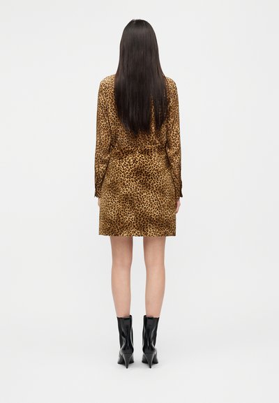 Φόρεμα με λεοπάρ σχέδιο, μακριά μανίκια, ελαστική μέση και κοντό τελείωμα. Φορεμένο με μαύρα μποτάκια με τακούνι και στον αστράγαλο. Πλάτη σε απλό φόντο.