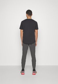 Czarna koszulka z krótkim rękawem zestawiona z szarymi zwężanymi spodniami. Strój charakteryzuje się luźnym krojem, wysokiej jakości materiałem oraz subtelnymi detalami.