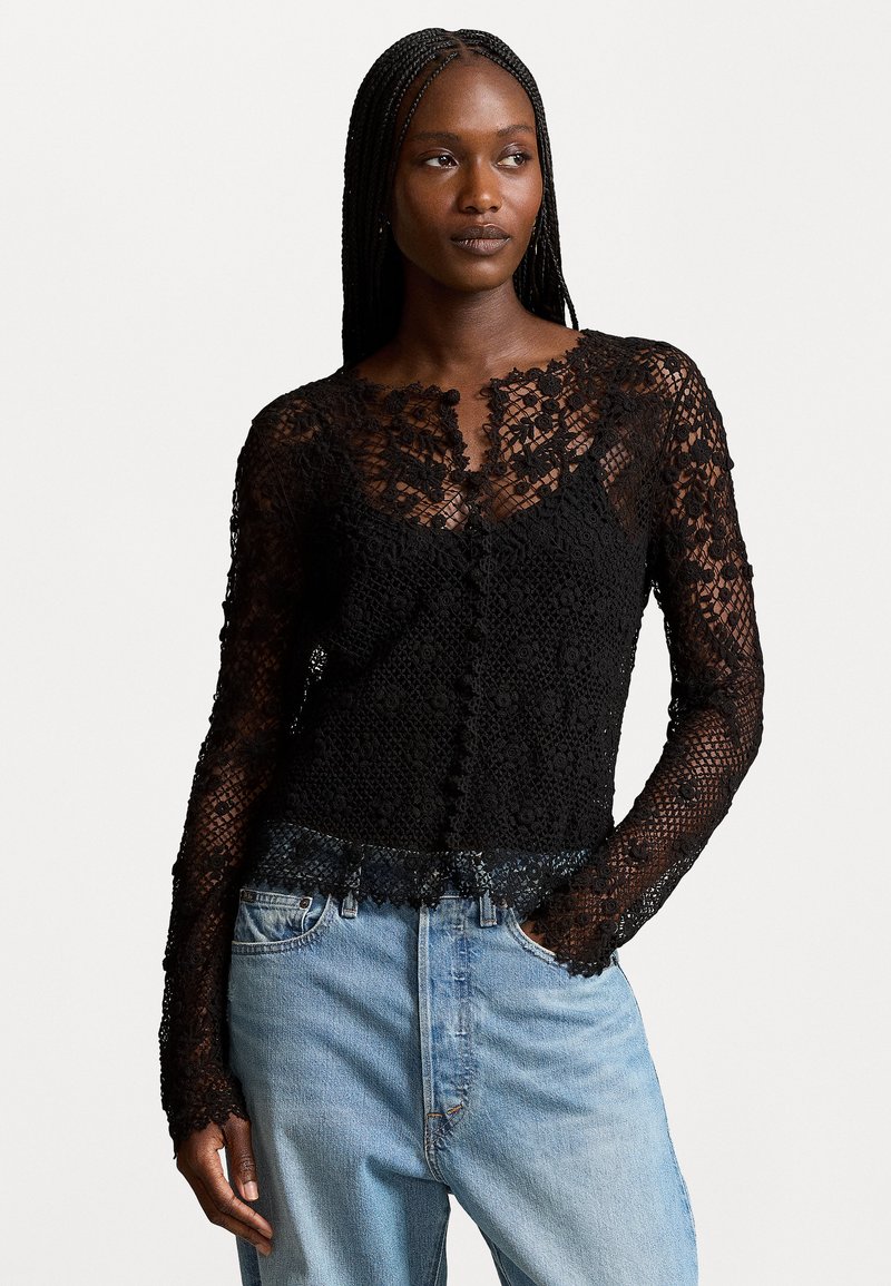 Black lace long-sleeve top with floral patterns, scalloped hem, and button details, paired with light blue high-waisted jeans.