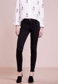 Jeans negros ajustados con una textura suave, que presentan un diseño clásico de cinco bolsillos y un cierre de botón, combinados con una camisa blanca con estampado de conejitos.