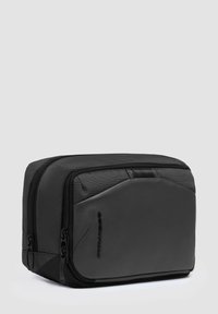 Borsa da viaggio nera con esterno in tessuto strutturato, pannello in pelle liscia, doppia cerniera e forma rettangolare compatta.