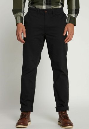 Zwarte katoenen chino's met een rechte snit, voorzien van opgerolde mouwen, een knoopsluiting en zijzakken. Gecombineerd met bruine veterschoenen.