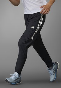 Schwarze Sporthosen mit weißen Seitenstreifen und einem Adidas-Logo, kombiniert mit hellblauen Laufschuhen mit Netz- und Gummidetails.