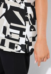 Top en blanco y negro con grandes letras abstractas. La tela es suave con un ligero brillo, y tiene aberturas laterales con costuras en contraste.