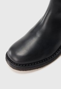 Must nahast saapakiil ümarate servadega ja paksu tekstuuriga kummist tallaga valgel taustal.