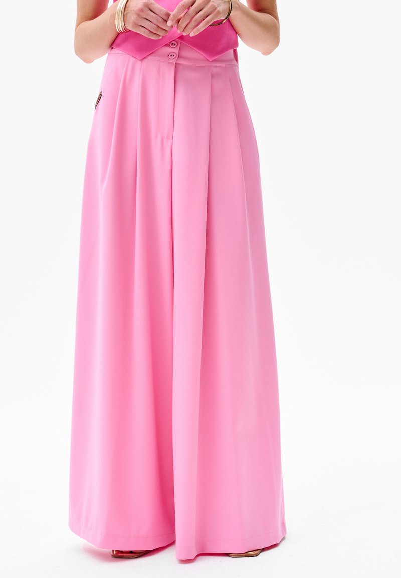 Pantalons larges roses avec une texture lisse, dotés d'un design plissé et d'une fermeture à boutons à la taille. Accentués par des poches latérales.