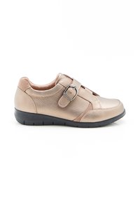 Scarpe in pelle beige con superficie texturizzata, dotate di una cinghia in Velcro e una fibbia argentata, montate su una suola in gomma nera.