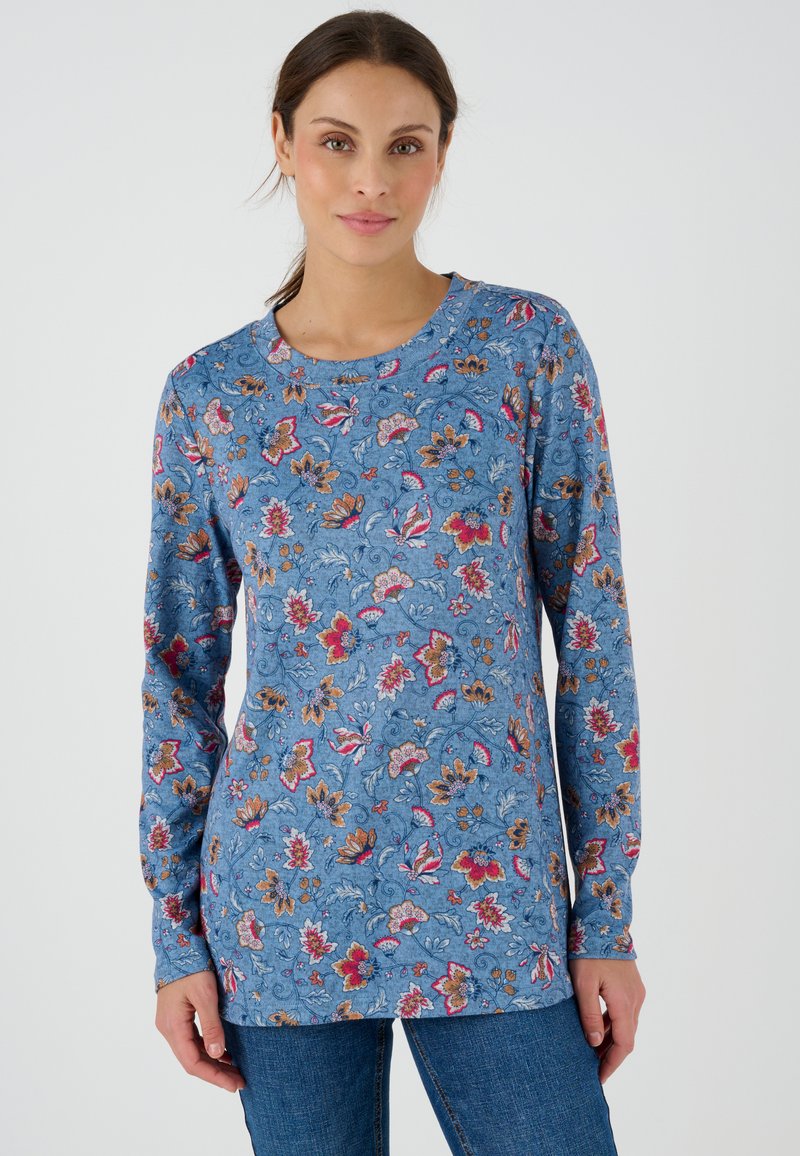 Maglia blu a maniche lunghe con motivi floreali in rosso, arancione e bianco. Collo rotondo e tessuto morbido. Abbinata a jeans di denim.