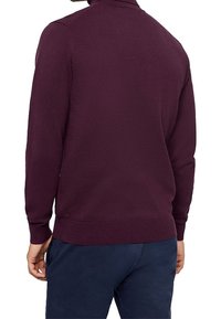 Homme portant un pull uni à manches longues violet foncé et un pantalon bleu foncé, vu de dos.