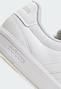 Baskets basses en cuir blanc avec semelle texturée, col rembourré, logo Adidas embossé sur le talon et imprimé sur la tige.